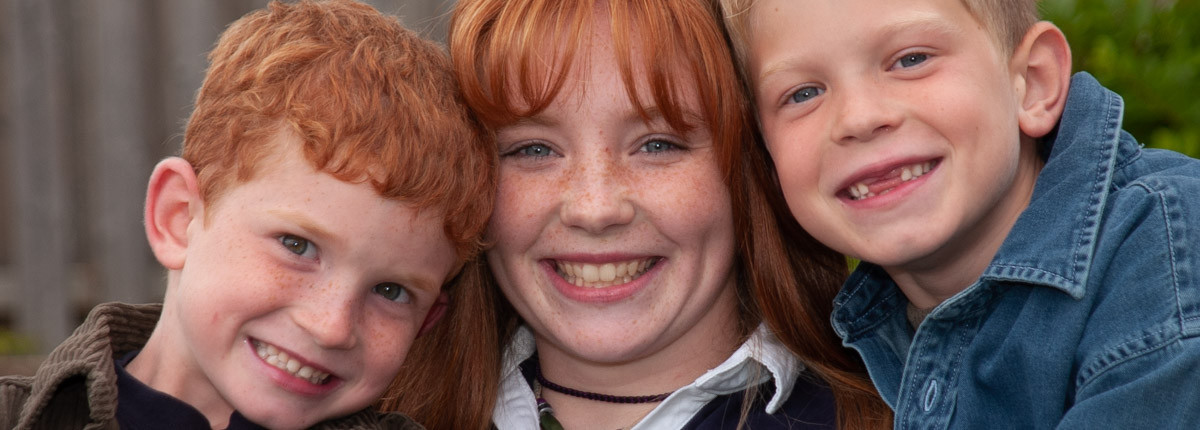 Casual outdoor portrait of three siblings huddled together with