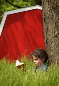 Young girl sitting on the ground in tall grass leaning against a